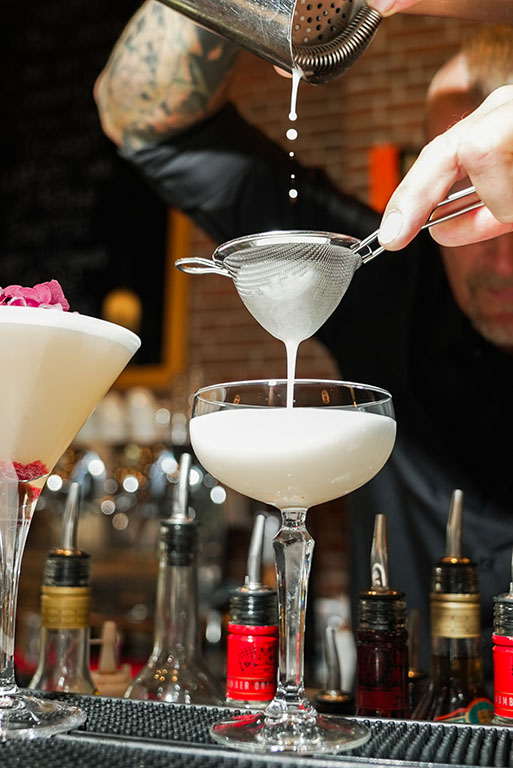 cocktail med skum skænkes og hældes gennem en si