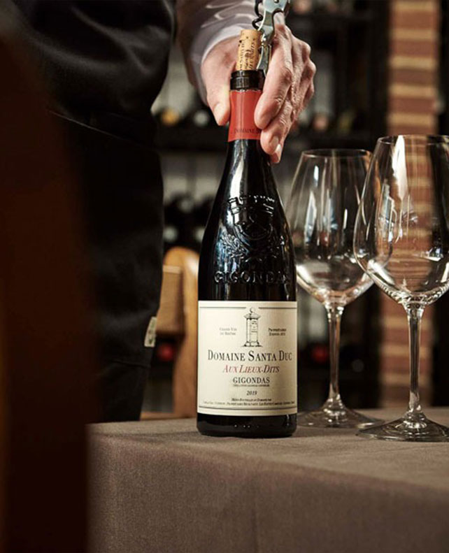 en flaske rødvin åbnes med poptrækker. Der er rødvinsglas på bordet.